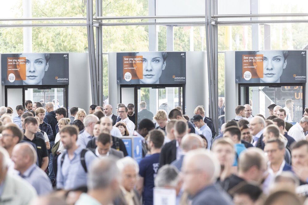 Eine große Menschenmenge bei der automatica 2023 in einem geschlossenen Raum mit sichtbaren Bannern im Hintergrund, die auf die automatica 2025 hinweisen.