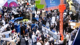 Densely packed trade fair hall with numerous booths for digital or technological solutions, where visitors interact, watch presentations, and work with displays.