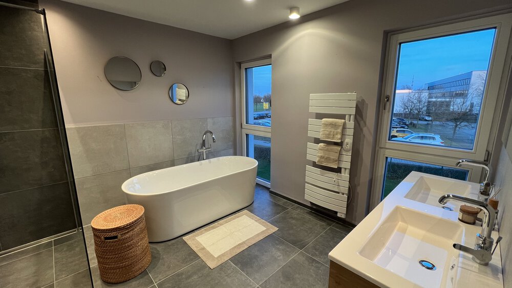 Modernes Badezimmer mit freistehender Badewanne, Doppelwaschbecken, Spiegeln und Fenster mit Blick nach draußen.