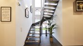 Moderne Metalltreppe mit Holzstufen in einem hellen Flur. Pflanzen und gerahmte Bilder an den Wänden.