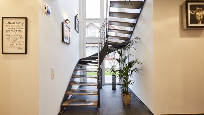 Moderne Metalltreppe mit Holzstufen in einem hellen Flur. Pflanzen und gerahmte Bilder an den Wänden.
