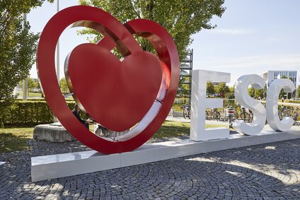 Der Schriftzug „ESC“ in weißen Buchstaben und mit einem großen abstrakten roten Herz davor steht neben dem Messesee der Messe München.
