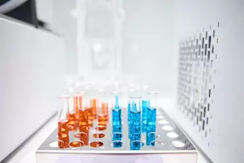 Test tubes stand in a holder. They are filled with a liquid - one part bright orange, one part bright blue.