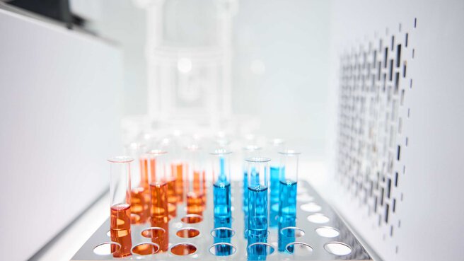 Test tubes stand in a holder. They are filled with a liquid - one part bright orange, one part bright blue.