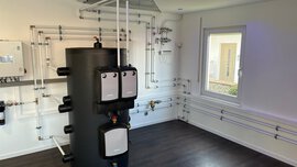 Moderne Kesselanlage mit freiliegenden Rohren in einem sauberen, hellen Raum mit weißen Wänden und einem Fenster.