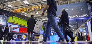 Frog's-eye view of a hall at transport logistic shows visitors with bags in their hands walking past various trade fair stands.