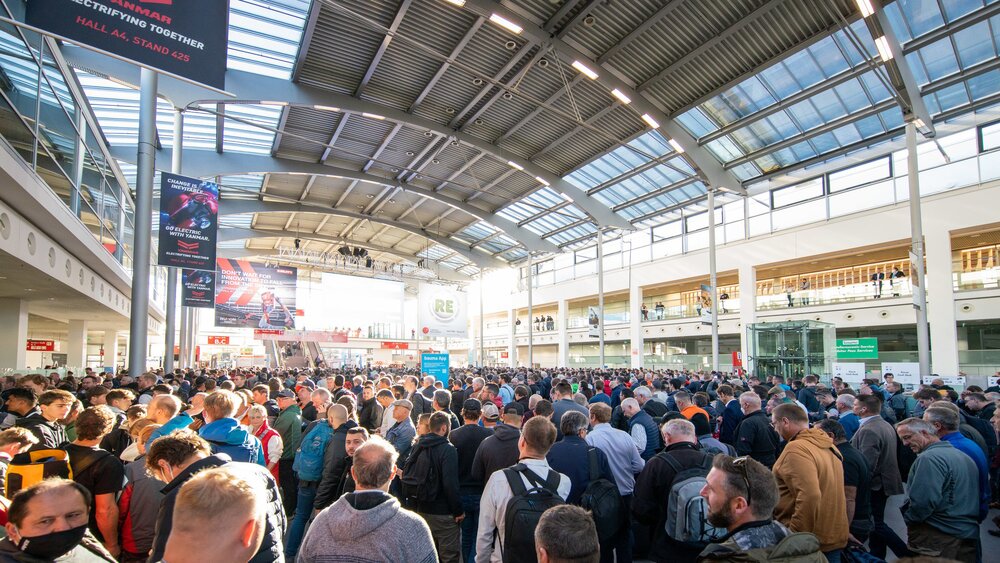 A large crowd gathers under a high, bright atrium roof with banners and stands.