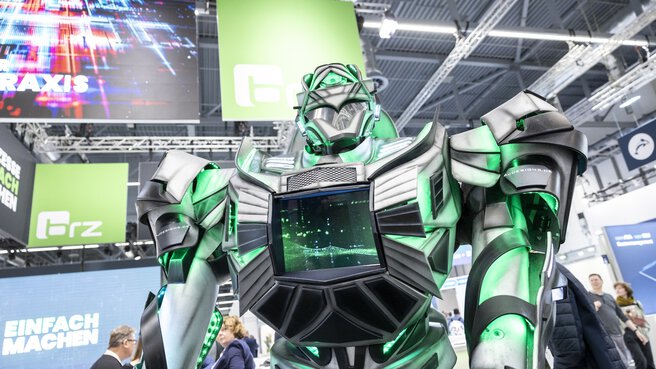 A large futuristic robot with green accents and a screen on its chest stands in an exhibition hall.