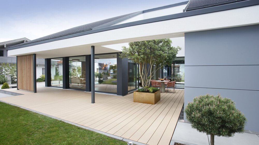 Modernes Haus mit großen Glastüren, Holzterrasse, Pflanzkübeln und kleinem Rasen davor.