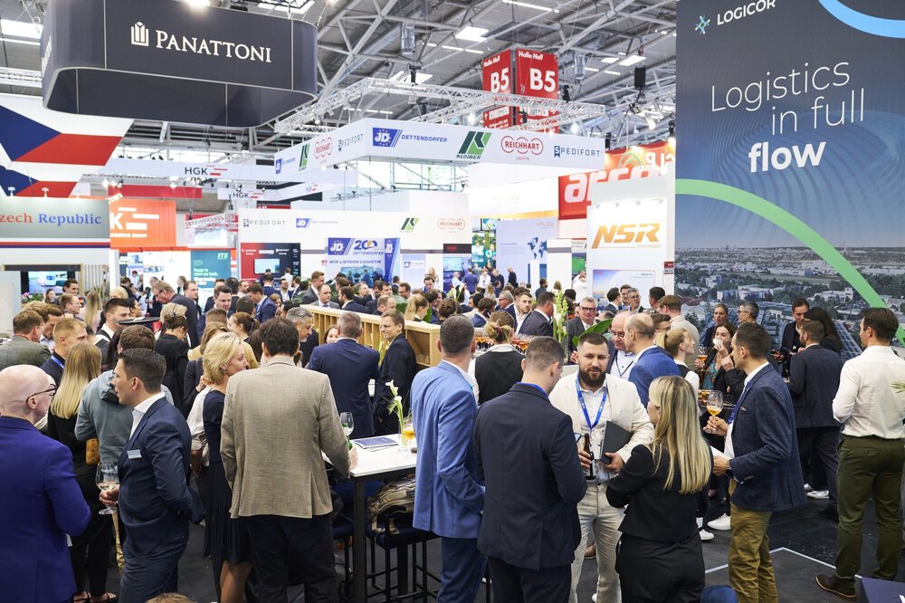 Eine große Menschenmenge versammelt sich auf einer belebten Logistikmesse mit Ständen und Bannern verschiedener Unternehmen.
