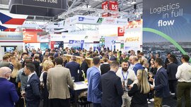 Eine große Menschenmenge versammelt sich auf einer belebten Logistikmesse mit Ständen und Bannern verschiedener Unternehmen.