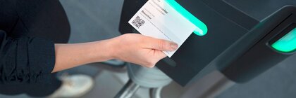 A ticket with a QR code is scanned by hand at a barrier under a green traffic light.