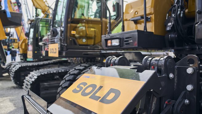 Baumaschine mit „SOLD“-Schild im Vordergrund, weitere verkaufte Bagger im Hintergrund.