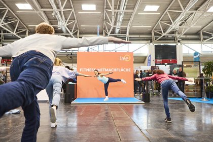 Trainer leads a fitness session on the hands-on area at the “f.re.e” trade fair, while visitors actively participate. Other visitors watch from outside.