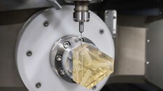 A CNC machine mills complex openings and connections into a translucent yellow block of material.