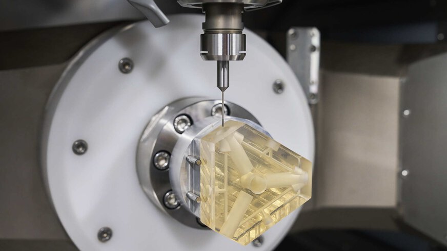 A CNC machine mills complex openings and connections into a translucent yellow block of material.
