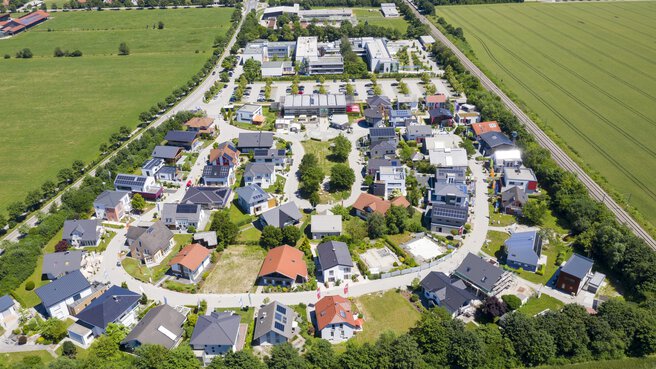 Luftaufnahme des Bauzentrum Poing mit grünen Feldern und Straßen, die moderne Häuser und Gebäude umgeben.