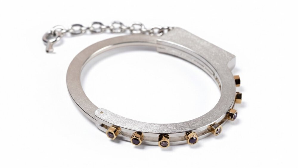 A silver bangle bracelet set with nut-shaped diamonds and a short chain, which is vaguely reminiscent of handcuffs.