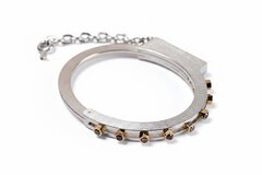 A silver bangle bracelet set with nut-shaped diamonds and a short chain, which is vaguely reminiscent of handcuffs.