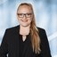 Frau mit langen Haaren und Brille, trägt einen schwarzen Blazer und lächelt.
