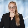 Frau mit langen Haaren und Brille, trägt einen schwarzen Blazer und lächelt.