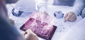 Two people are sitting at a table with construction plans. Between them is a tablet with the purple outline of a 3D house protruding from it.