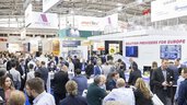 Ein gut besuchter Bereich der productronica, in dem sich Besucher in Gruppen austauschen, während über ihren Köpfen Banner mit Logos der Aussteller prangen.