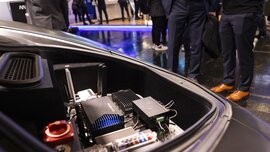 Close-up of a trunk in which electronic devices and tools can be seen, with people standing in the background.