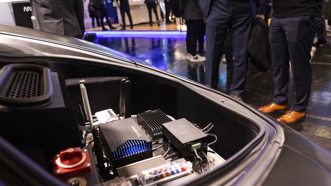 Close-up of a trunk in which electronic devices and tools can be seen, with people standing in the background.