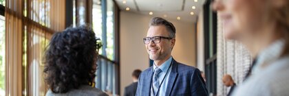 Ein Mann im Anzug hält eine Kaffeetasse und schüttelt einer Frau bei einer geschäftlichen Veranstaltung die Hand.
