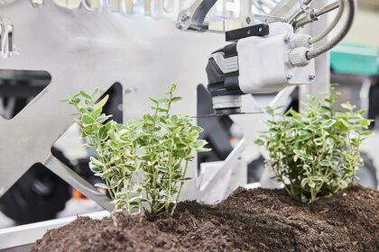 Ein Roboterarm kümmert sich um Pflanzen in einem Schaukasten auf einem Messestand.