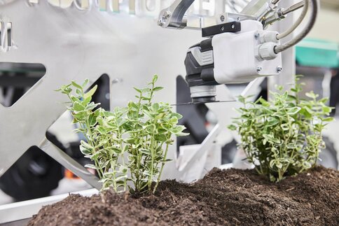 A robotic arm looks after plants in a display case at a trade fair stand.