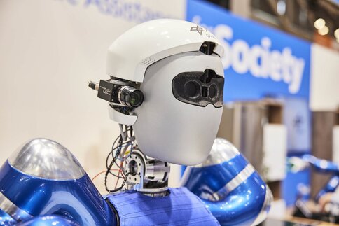 A humanoid robot with a white helmet and blue arms is displayed at a technology exhibition.