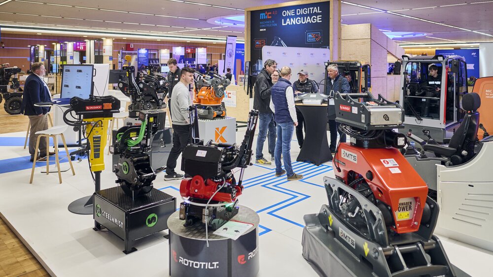 MiC 4.0 Messestand mit Baumaschinen-Anbaugeräten und mehreren Besuchern.