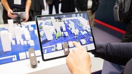 Person using a tablet on which a 3D augmented reality map of a city with various buildings is displayed.