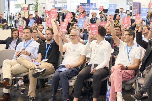 Teilnehmende stimmen beim Pitch-Wettbewerb im Founders Forum der World of Quantum 2025 aktiv mit farbigen Karten ab.