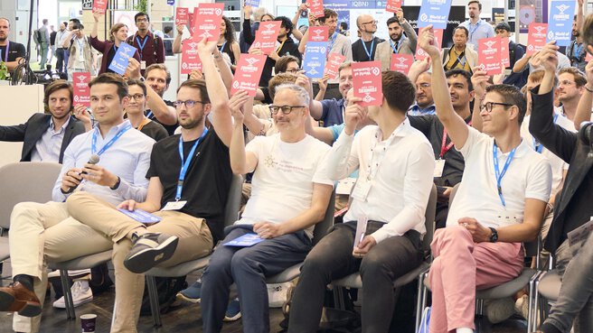 Teilnehmende stimmen beim Pitch-Wettbewerb im Founders Forum der World of Quantum 2025 aktiv mit farbigen Karten ab.