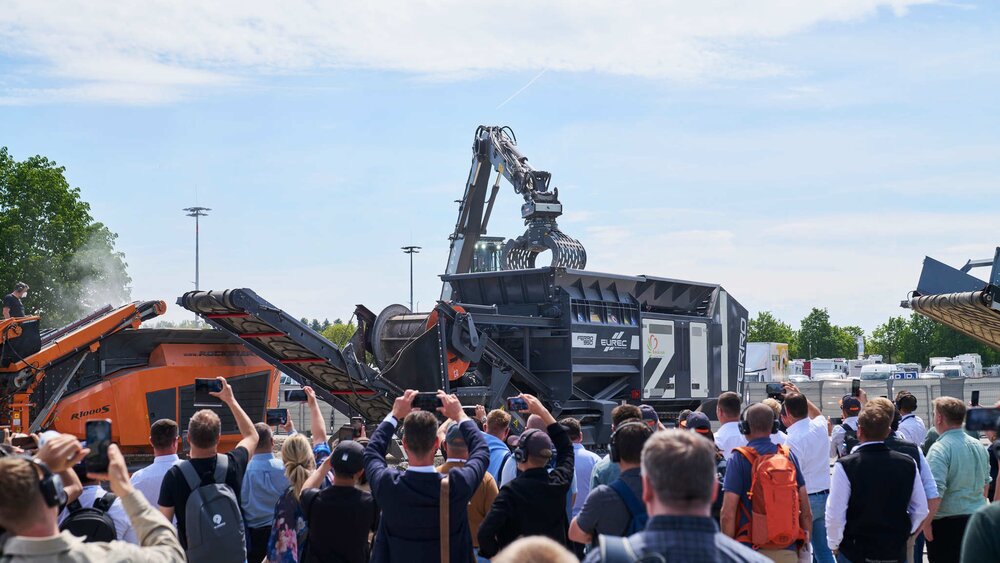 A group of spectators photographing and filming a live demonstration of mobile recycling shredders in the IFAT outdoor area.