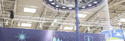 Großer Mast an einem Messestand mit einem kreisrunden Ring aus LED Leuchten vor denen ein Vorhang aus Wassertropfen herabrieselt.