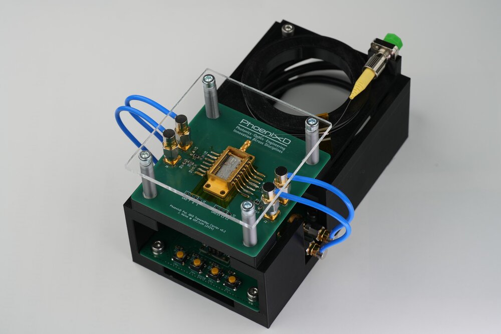 Photonics demonstrator by PhoenixD featuring an optical chip on a green PCB with blue connector tubes