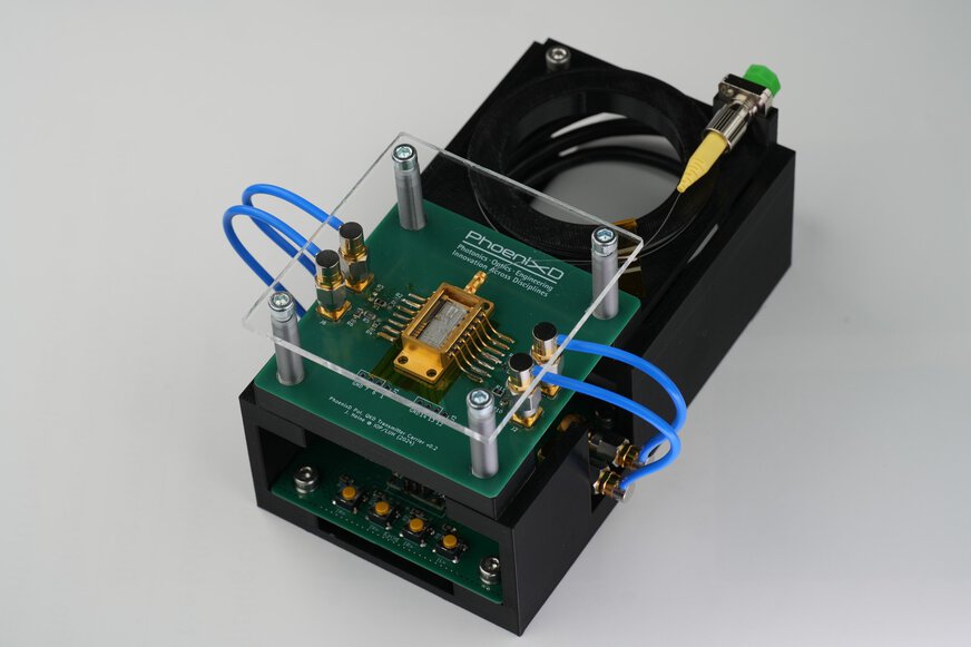 Photonics demonstrator by PhoenixD featuring an optical chip on a green PCB with blue connector tubes