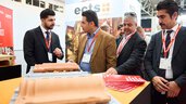Trade fair visitors in discussion at a booth, examining roof tile exhibits together.