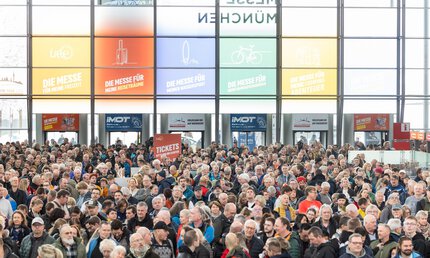 Numerous visitors to f.re.e are standing in the entrance area of the trade fair. Behind them, you can see the entrances and a large window front.