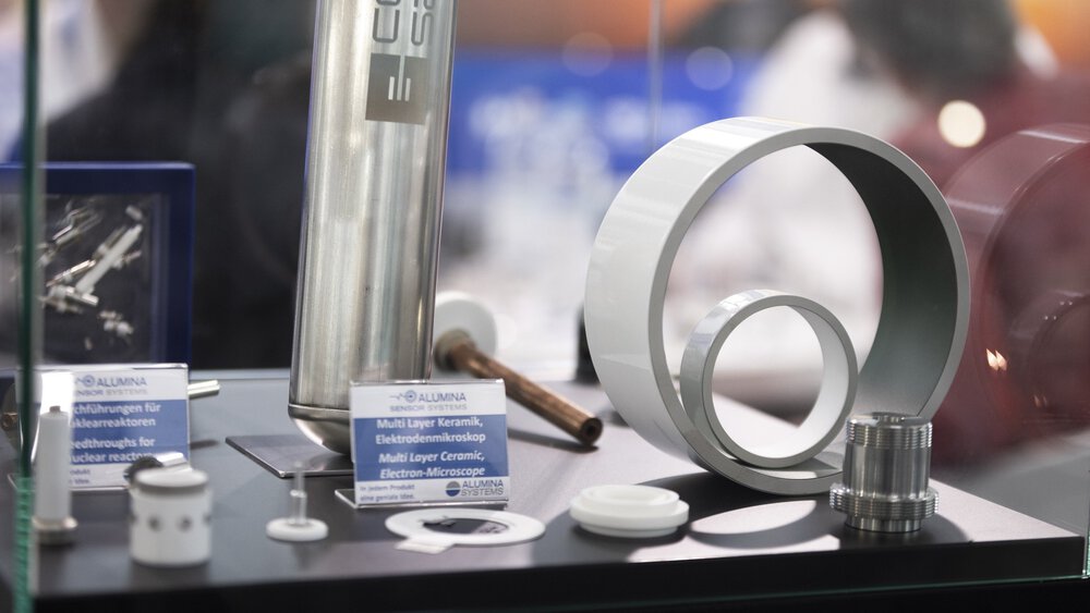 Vitrine mit diversen hellen Ausstellungsstücken, zylinderförmig, mit Gewinden und Ausstellungsschildern, auf denen z.B. „Multi Layer Keramik, Elektrodenmikroskop“ steht.