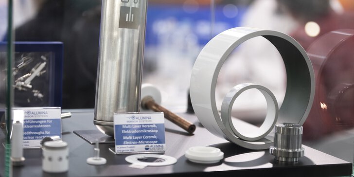 Vitrine mit diversen hellen Ausstellungsstücken, zylinderförmig, mit Gewinden und Ausstellungsschildern, auf denen z.B. „Multi Layer Keramik, Elektrodenmikroskop“ steht.