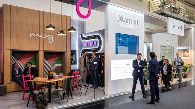 Menschen unterhalten sich an einem modernen Messestand mit Sitzgelegenheiten und Ausstellungsstücken.