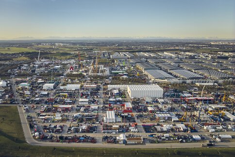 Extensive bauma trade fair grounds from a bird's-eye view with numerous construction machines and exhibition tents under a blue sky.