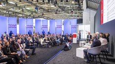 A panel discussion at EXPO REAL in Munich on the topic of “Flexible Housing.” Several experts are seated on stage, speaking to a large audience listening attentively. In the background, illuminated panels display the words “Flexible Housing