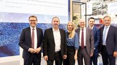 Eine Gruppe von sechs Personen in Business-Kleidung, darunter Hubert Aiwanger und Stefan Rummel, posiert lächelnd vor einer Infowand zur Spotlight Area Wasserstoff.