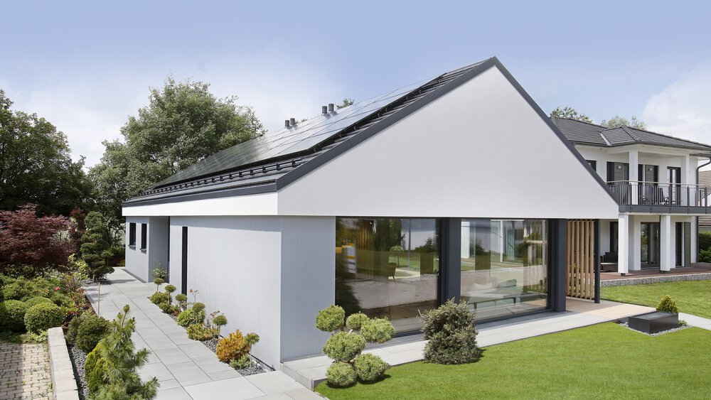 Modernes weißes Haus mit großen Fenstern, Satteldach und angelegtem Garten im Vordergrund.
